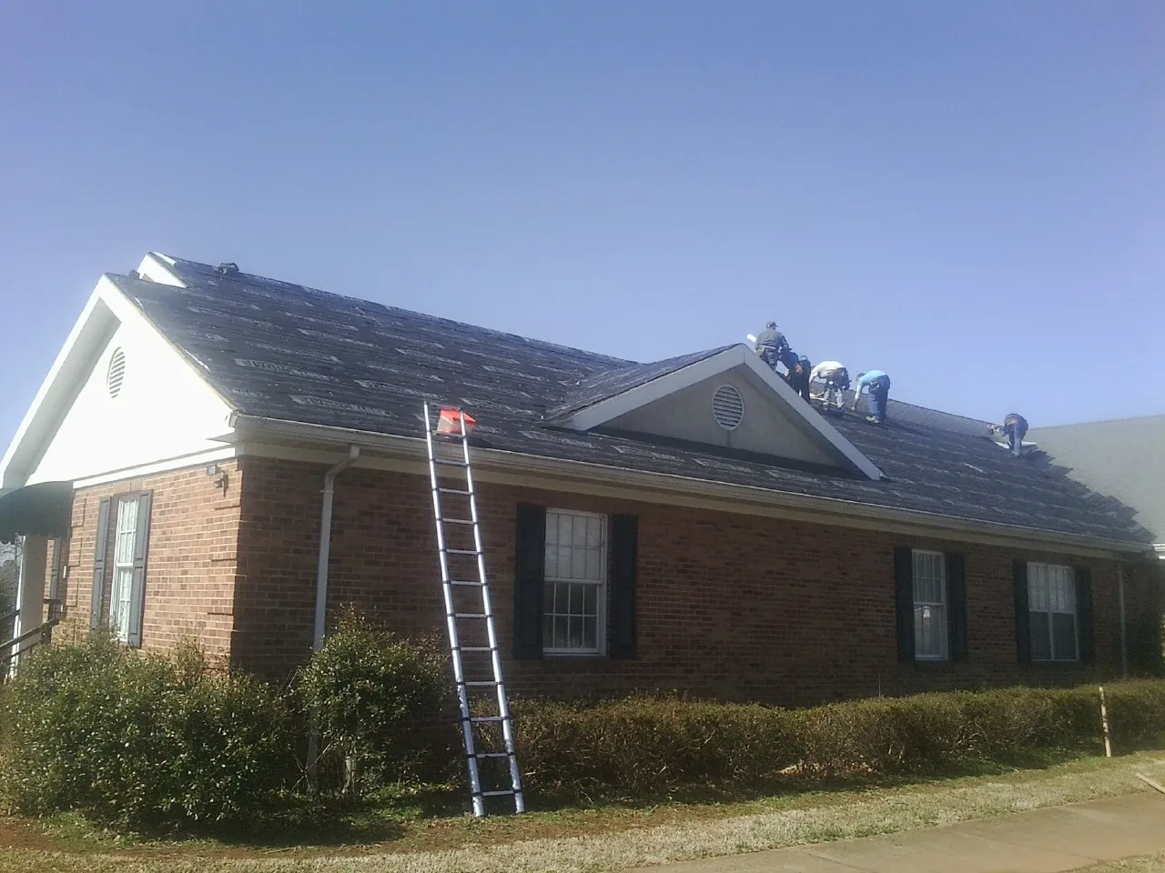 Crew tearing shingles off a brick ranch roof with a ladder set — Emergency Roof Repair work by our crew in Neshanic Station