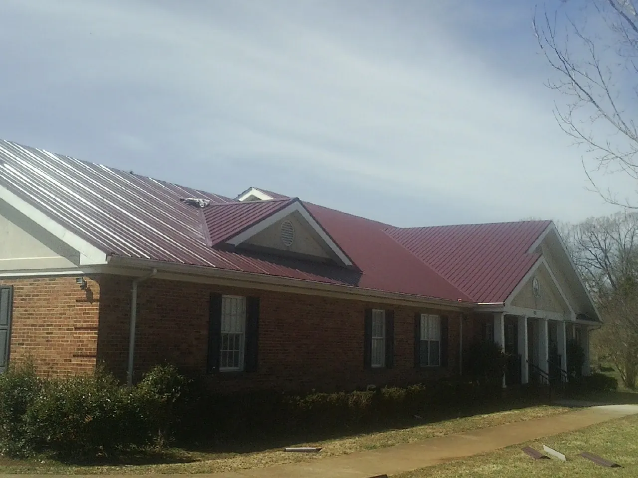 Red metal roof with gabled entries on a long brick building, from a Hail Damage Roof Repair job in Neshanic Station