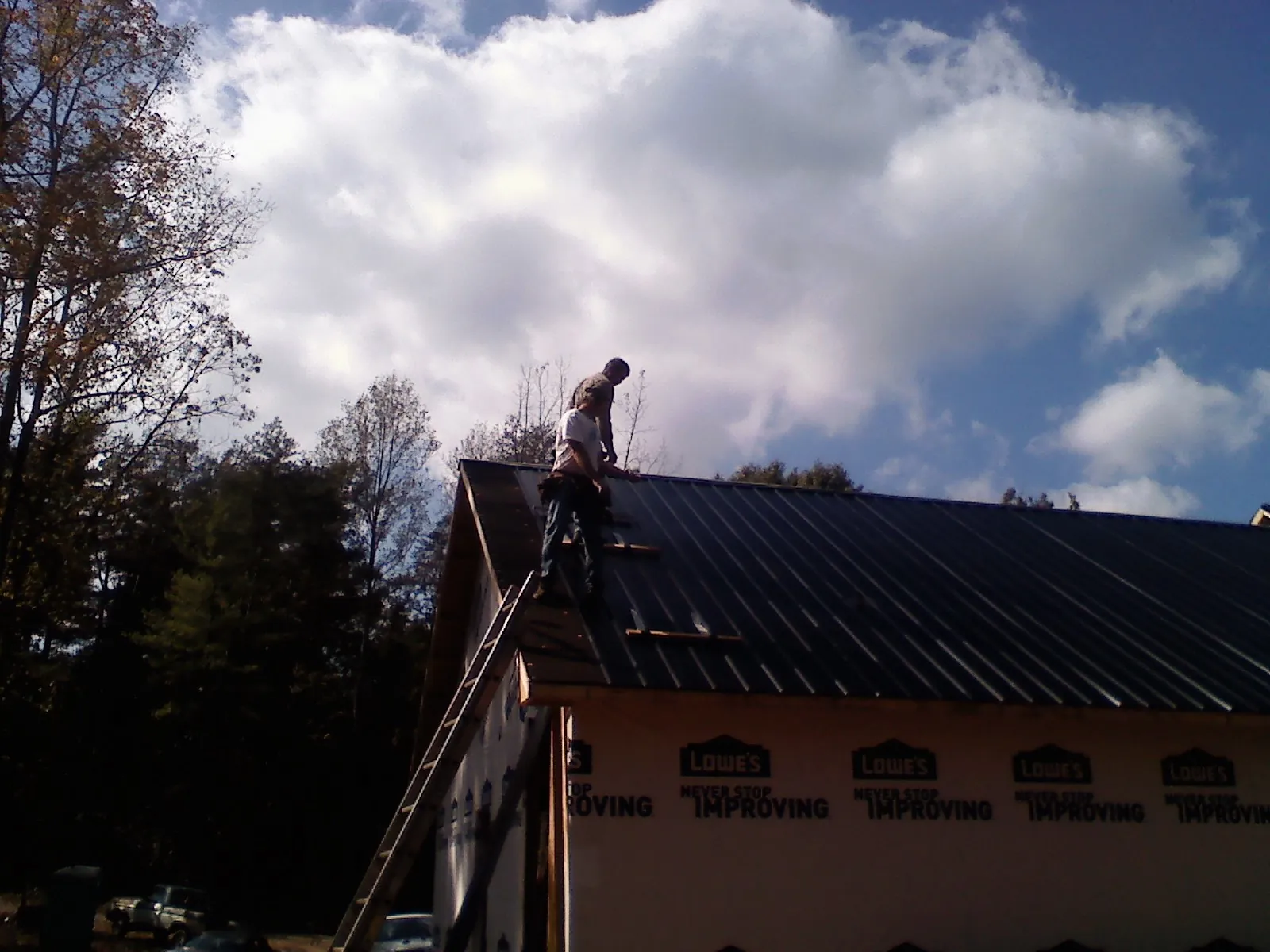 Roofer fastening dark metal panels high against a cloudy sky, from a Roof Inspection job in Neshanic Station