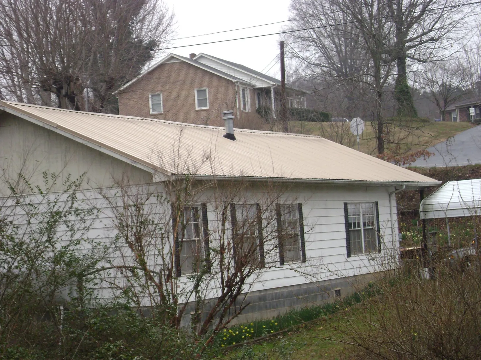 Tan metal roof on a white sided house set into a hillside — Commercial Roofing by Roofing Brothers in Neshanic Station